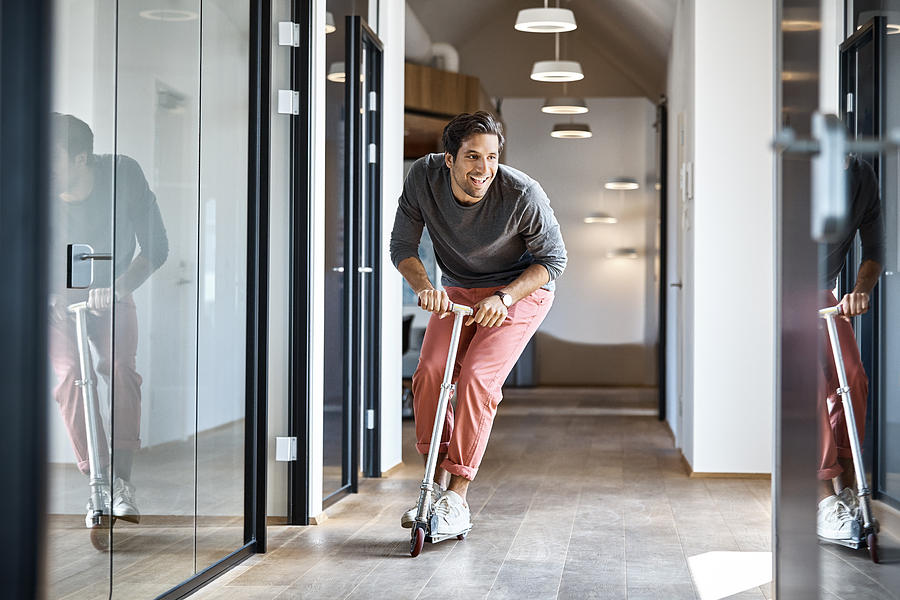 Businessman enjoying on push scooter in office Photograph by Morsa Images
