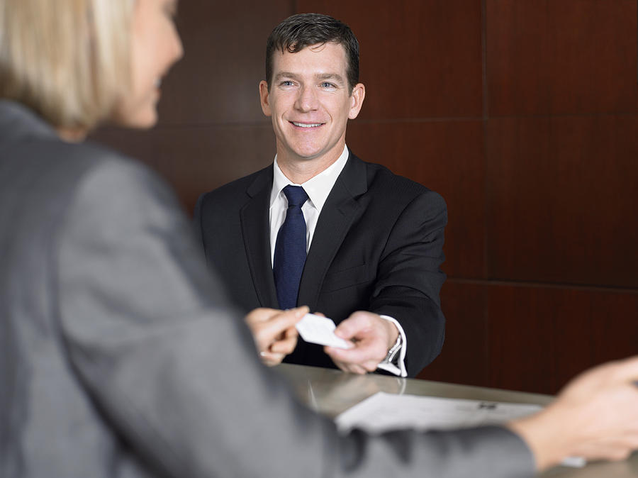 Businessman Giving a Receptionist His Business Card Photograph by Digital Vision.
