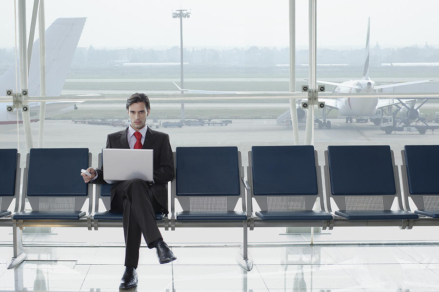 Businessman in airport with laptop and mobile phone Photograph by Floresco Productions