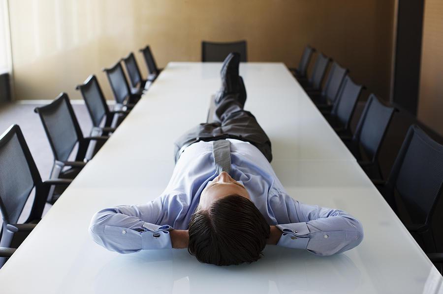 Businessman laying on conference room table Photograph by Tom Merton