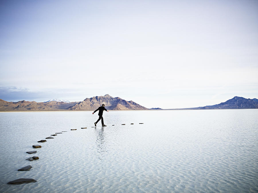 Businessman leaping between stones on pathway in l Photograph by Thomas Barwick