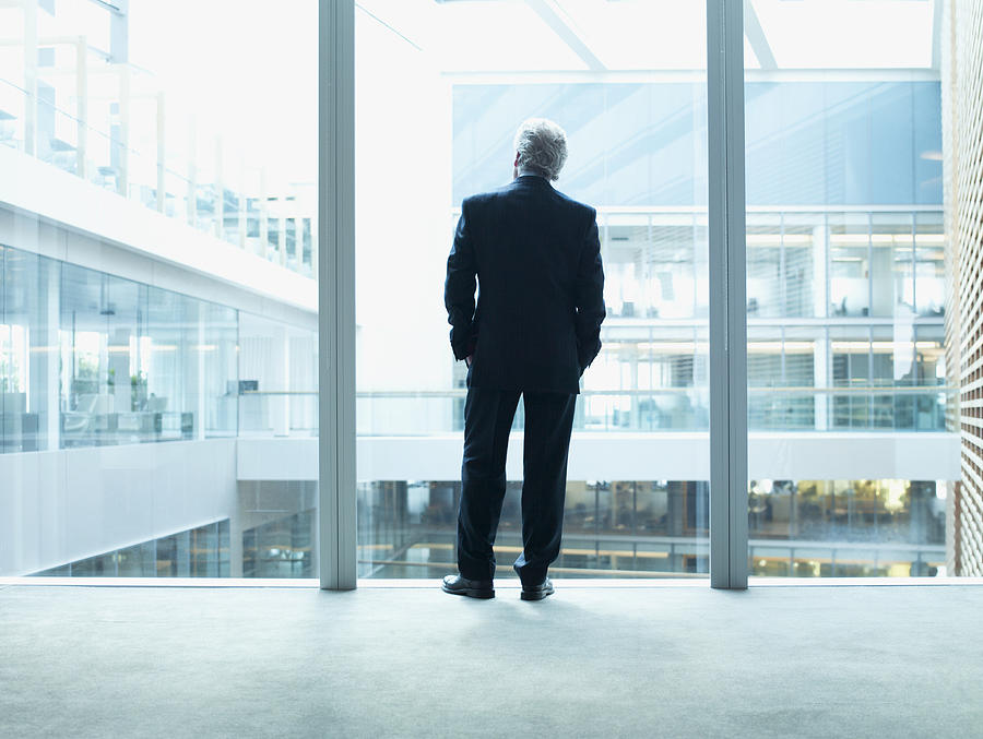 Businessman looking out glass wall in office Photograph by Martin Barraud