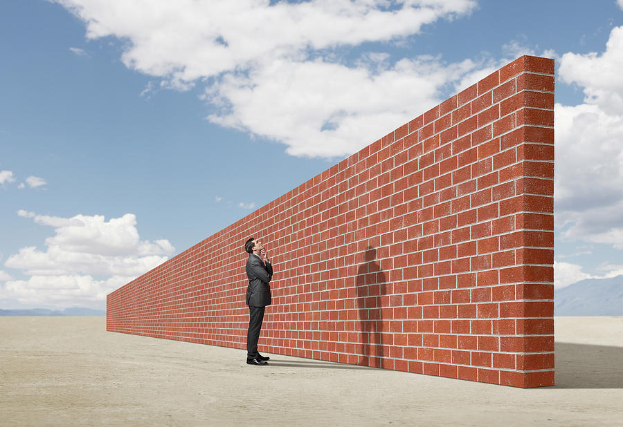 Businessman looking up at brick wall in middle of desert Photograph by Dny59