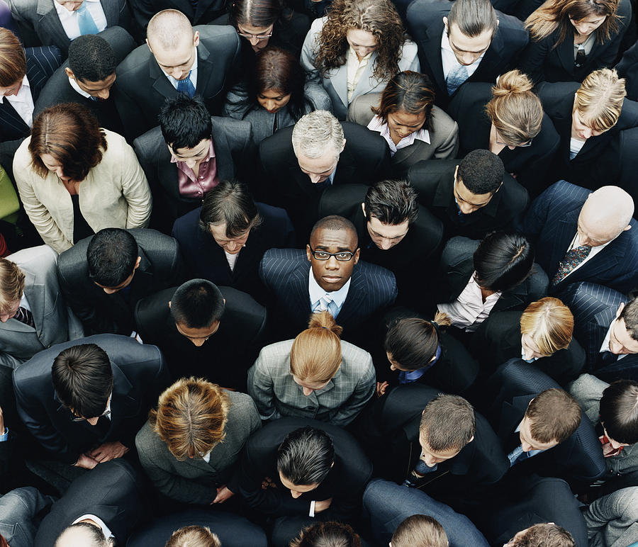 Businessman Looking up at Camera and Standing Outdoors Surrounded by a Large Group of Business People Photograph by Digital Vision.