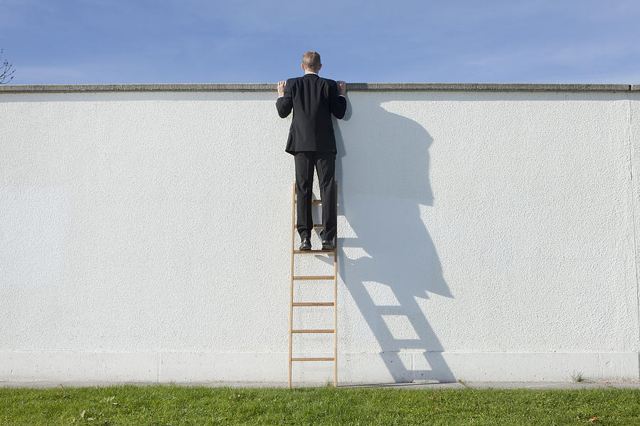 Businessman on ladder looking over wall Photograph by Johnny Valley