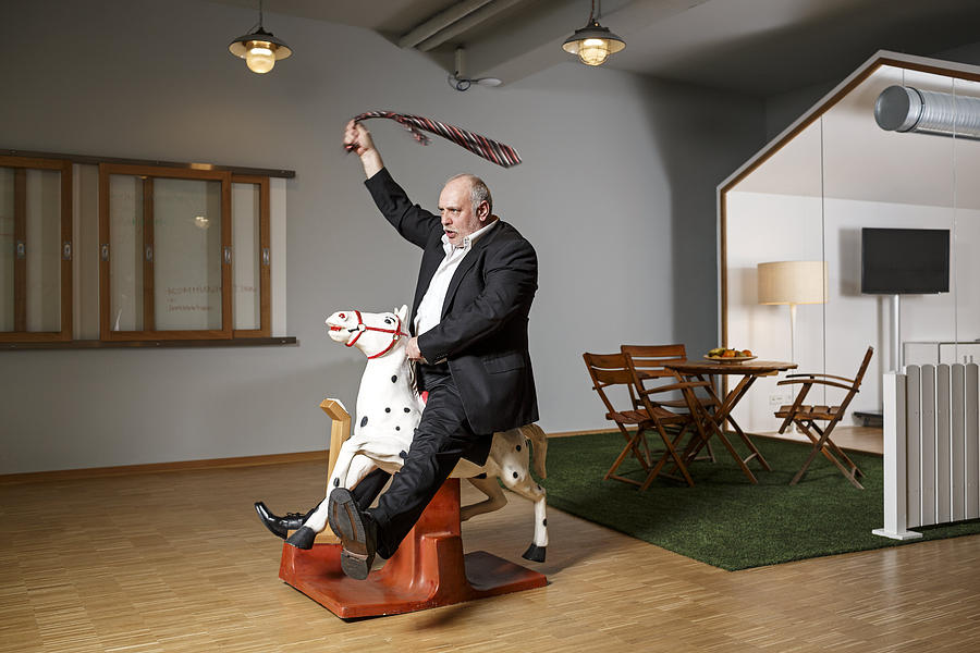 Businessman on rocking horse pretending to ride Photograph by Westend61