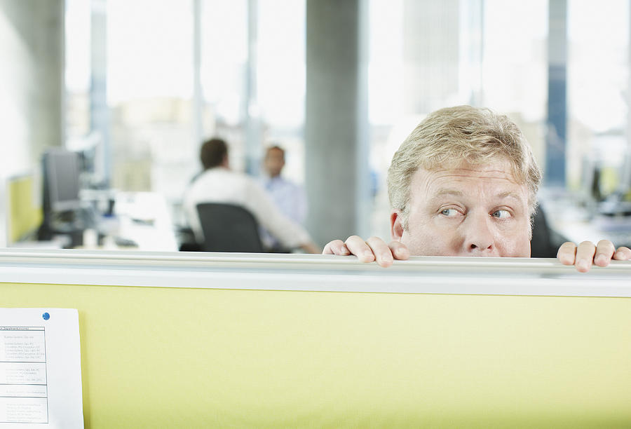 Businessman peering over cubicle wall Photograph by Paul Bradbury