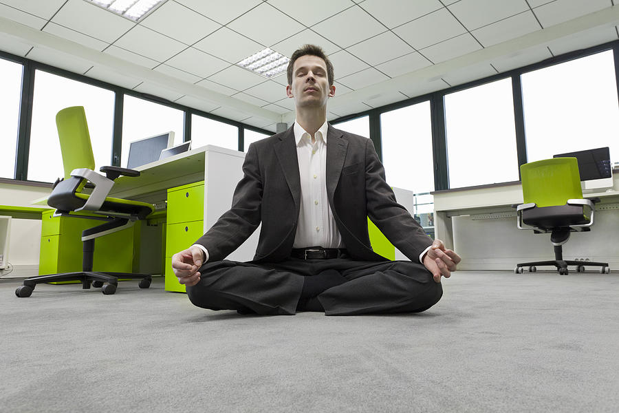 Businessman Practicing Meditation In Office Photograph by Paul Harizan