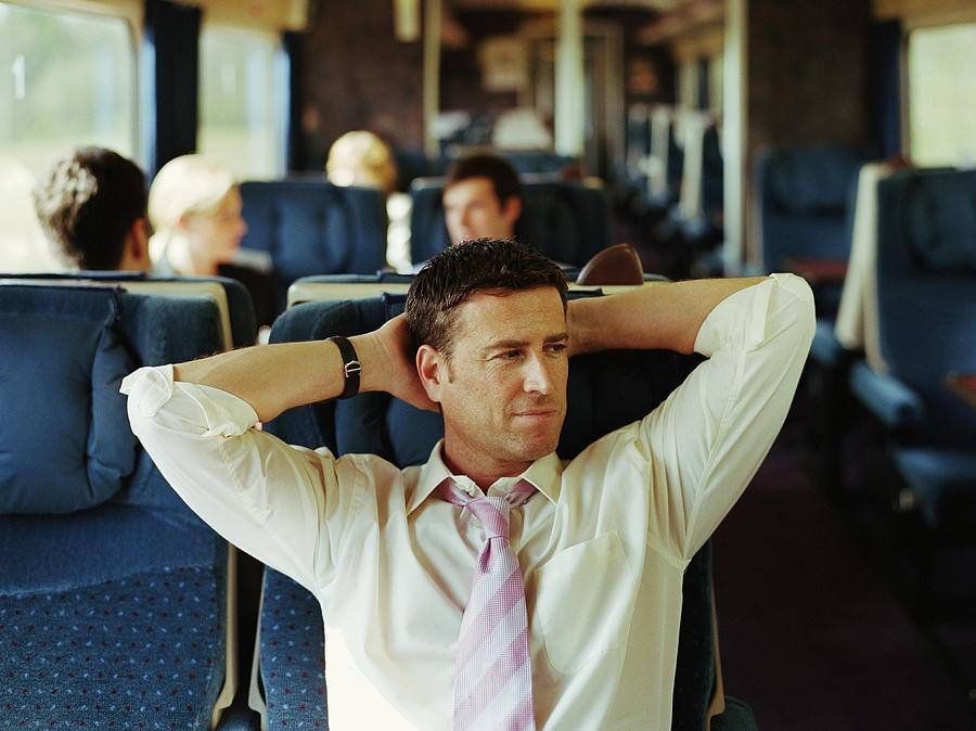 Businessman relaxing on train, hands behind head (focus on man) Photograph by Digital Vision