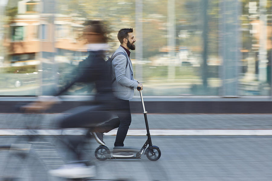 Businessman riding scooter along office building Photograph by Westend61