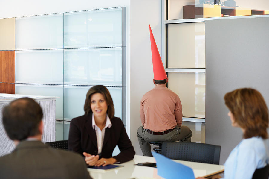 Businessman sat in corner with dunce cap Photograph by Image_Source_