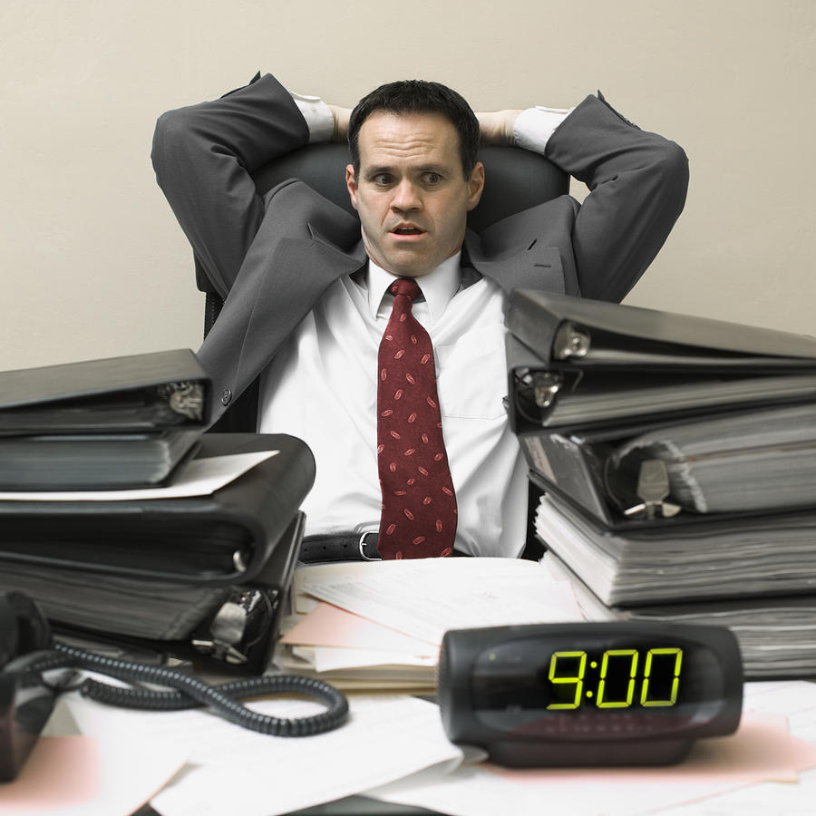 Businessman sitting behind a desk with his hands behind his head Photograph by Photodisc