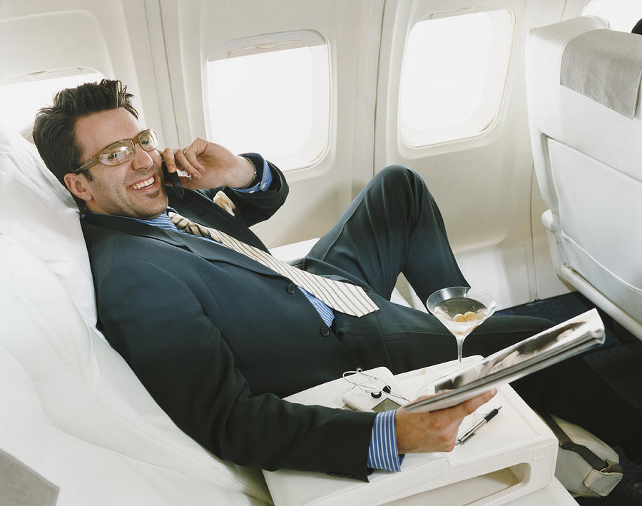 Businessman Sitting in an Aircraft Wearing Glasses and Holding a Magazine Photograph by Digital Vision.