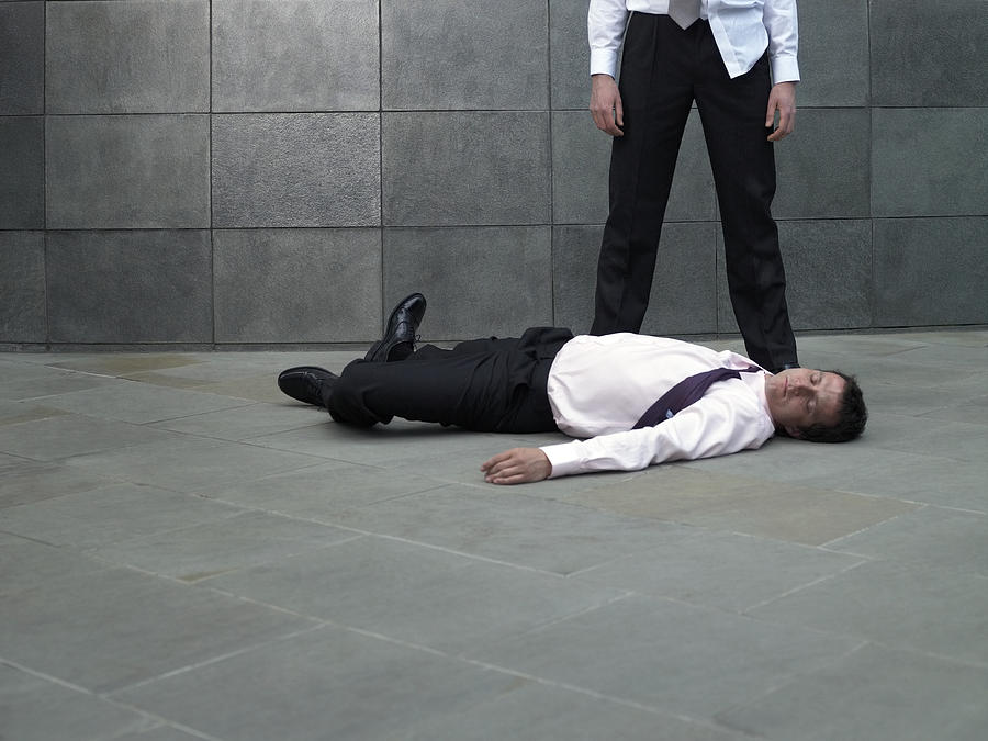 Businessman standing over colleague lying on pavement Photograph by Michael Blann