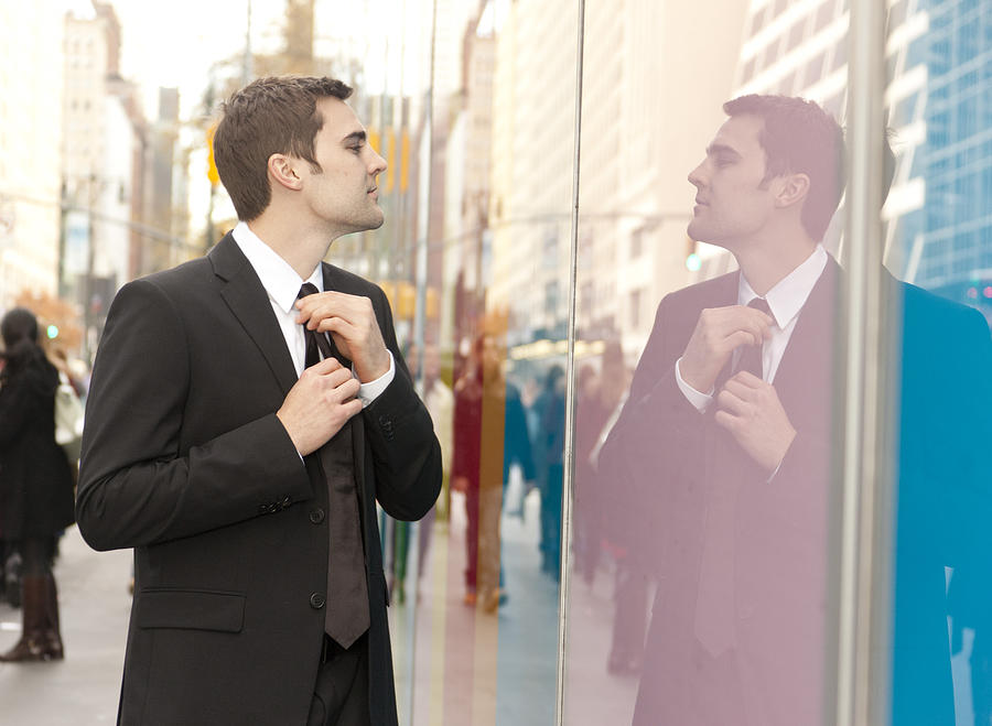 Businessman straightening his tie in reflection Photograph by Tooga