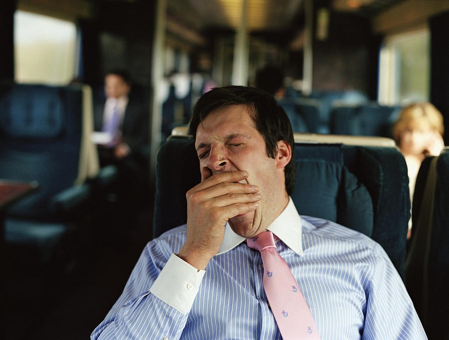 Businessman yawning on train (focus on man) Photograph by Digital Vision