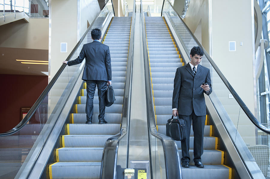 Businessmen standing on escalators Photograph by Jacobs Stock Photography Ltd