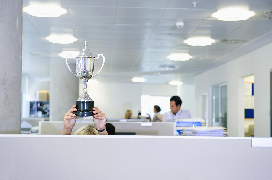 Businesswoman holding trophy over office cubicle Photograph by Jacobs Stock Photography Ltd