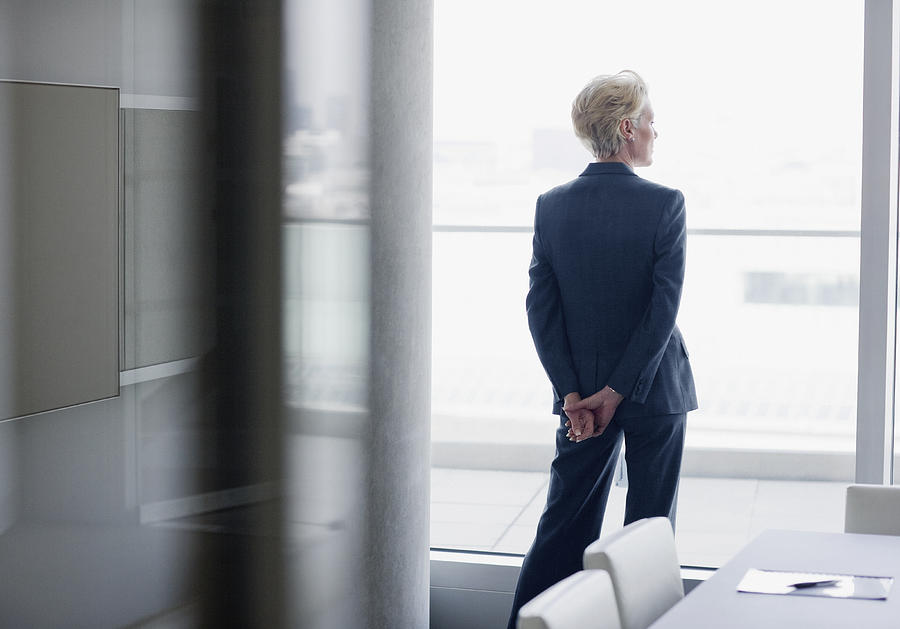 Businesswoman standing at window in office Photograph by Sam Edwards