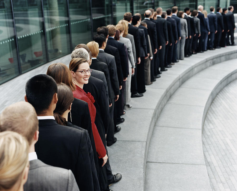 Businesswoman Standing Out in a Line of Business People Waiting Outdoors on a Step Photograph by Digital Vision.