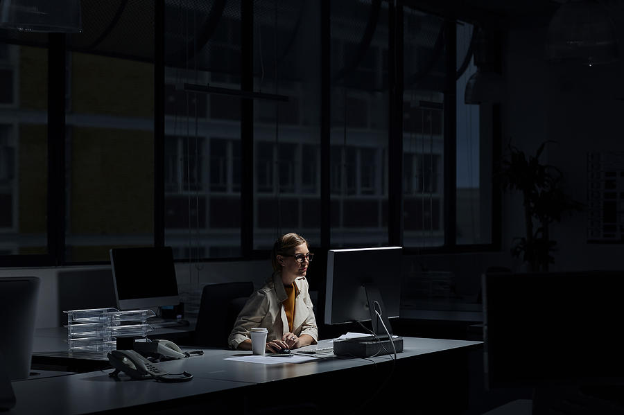 Businesswoman using computer in dark office Photograph by Morsa Images
