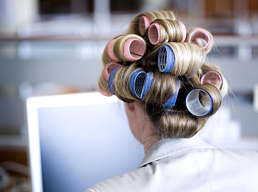 Businesswoman with hair on curlers in office, rear view Photograph by Roger Wright