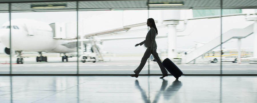 Businesswoman with suitcase in airport Photograph by Martin Barraud