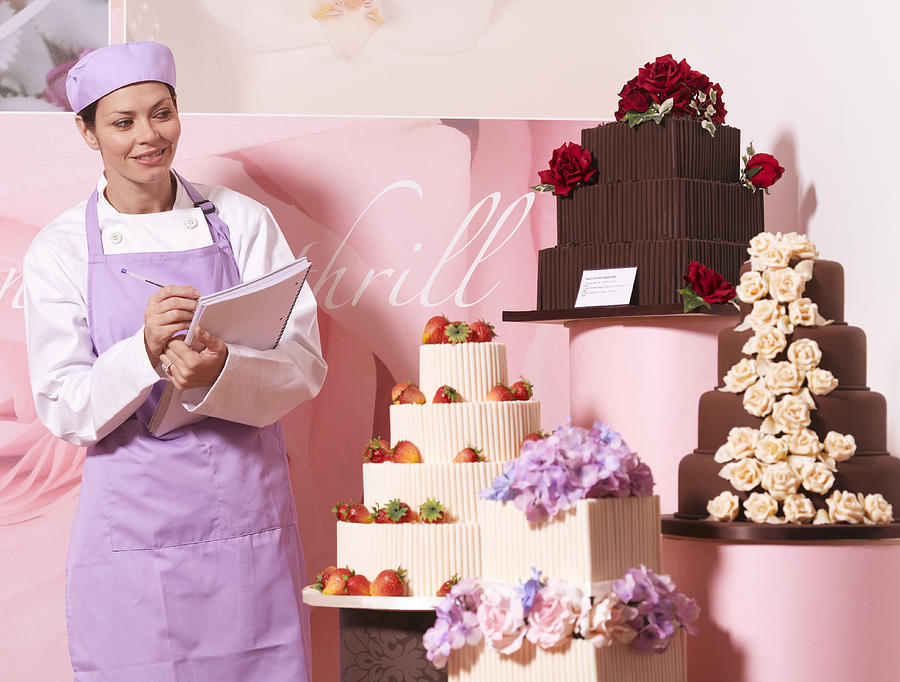 Cake maker in cake shop, holding notebook, smiling Photograph by Peter Dazeley