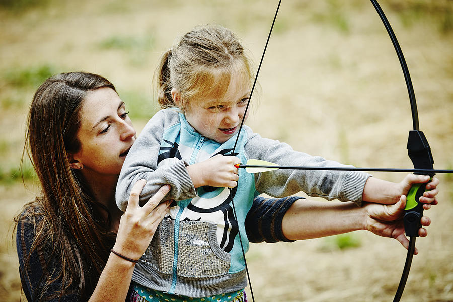 Camp counselor helping girl shoot bow and arrow Photograph by Thomas Barwick