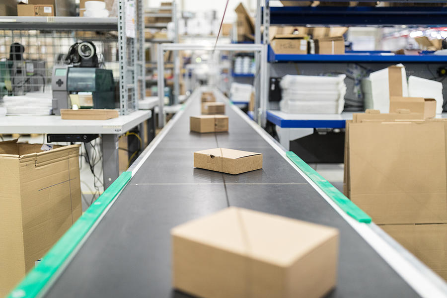 Cardboard boxes on conveyor belt at distribution warehouse Photograph by Alvarez