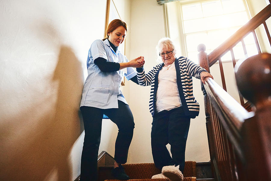 Caregiver helping senior woman walking down stairs Photograph by Dean Mitchell