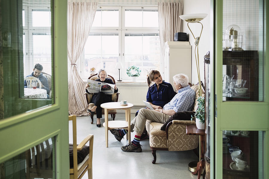 Caretakers with senior couple sitting in living room at nursing home Photograph by Maskot