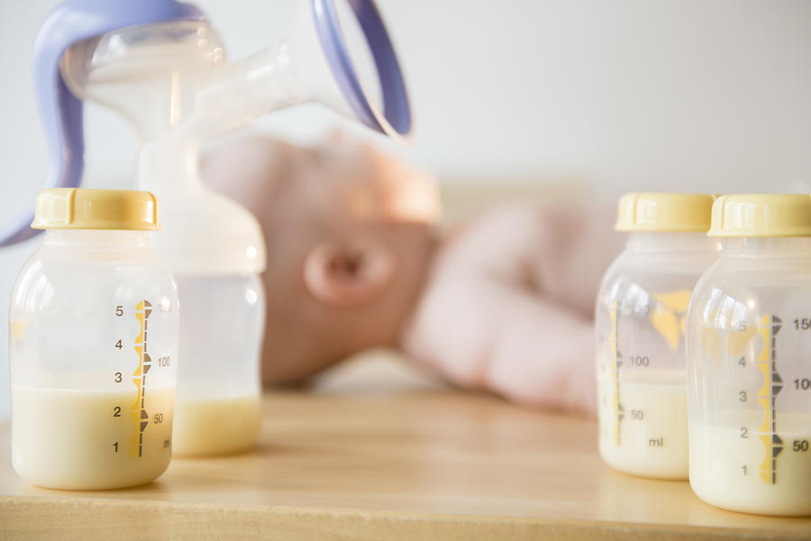 Caucasian baby boy laying near bottles of breast milk and breast pump Photograph by JGI/Jamie Grill