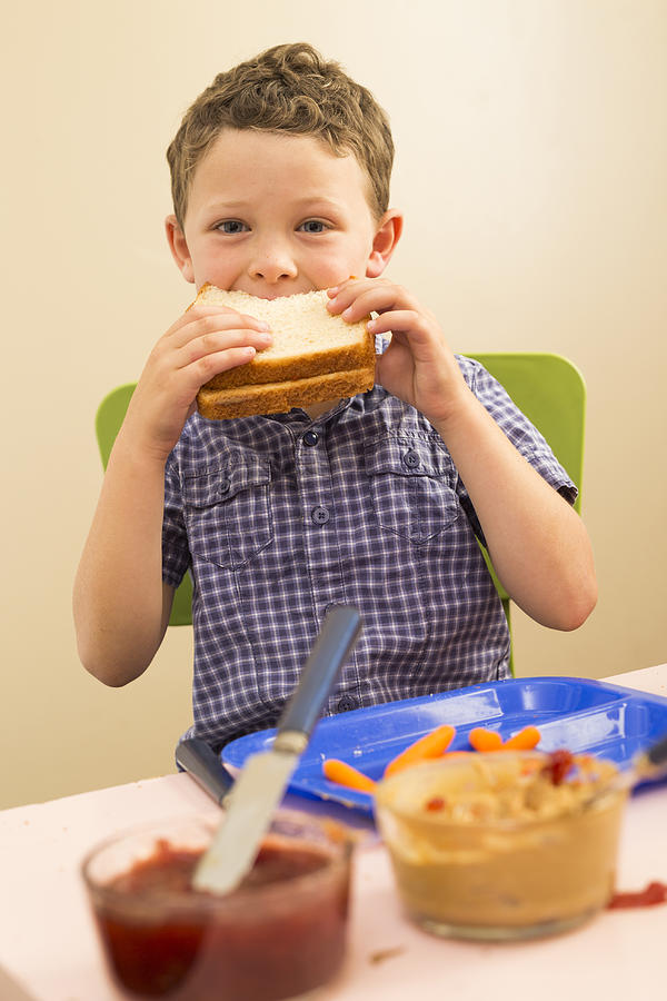 Caucasian boy eating sandwich in kitchen Photograph by Mike Kemp