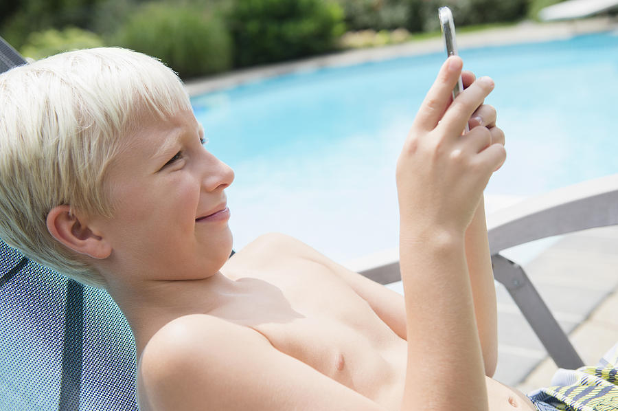 Caucasian boy using cell phone near swimming pool Photograph by JGI/Jamie Grill