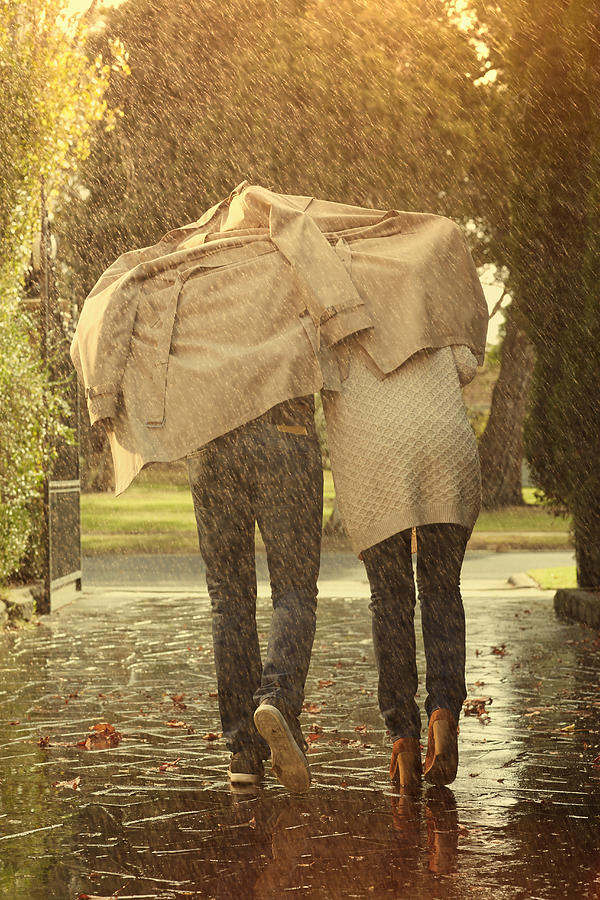 Caucasian couple running under coat in rain Photograph by Colin Anderson Productions pty ltd