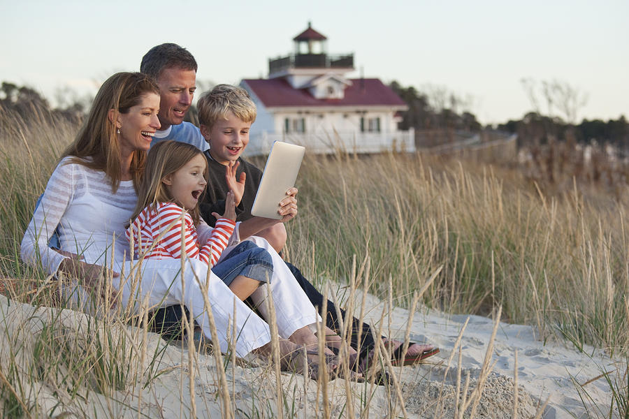 Caucasian family using digital tablet on beach Photograph by Ariel Skelley