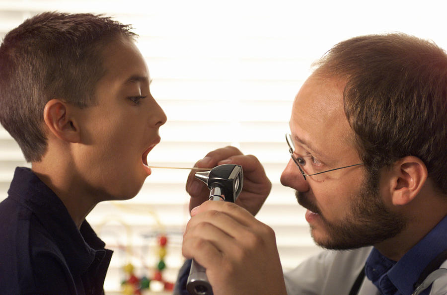Caucasian Male Pediatrician With Beard Examines The Throat Of A Young Boy Patient During A Check Up Photograph by Photodisc