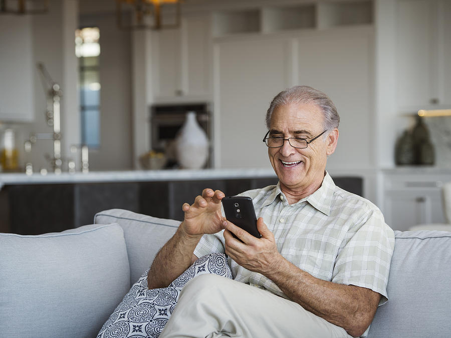Caucasian man sitting on sofa texting on cell phone Photograph by Erik Isakson