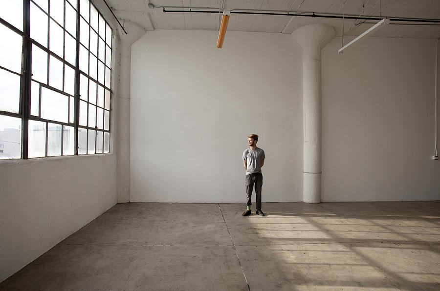 Caucasian man standing in empty loft Photograph by Kyle Monk