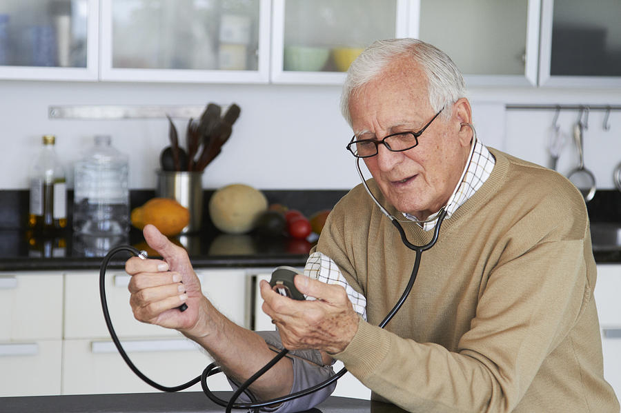 Caucasian man taking his own blood pressure Photograph by Rolf Bruderer