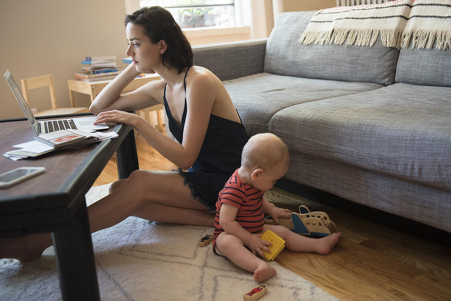 Caucasian mother sitting on floor using laptop near baby son Photograph by JGI/Jamie Grill