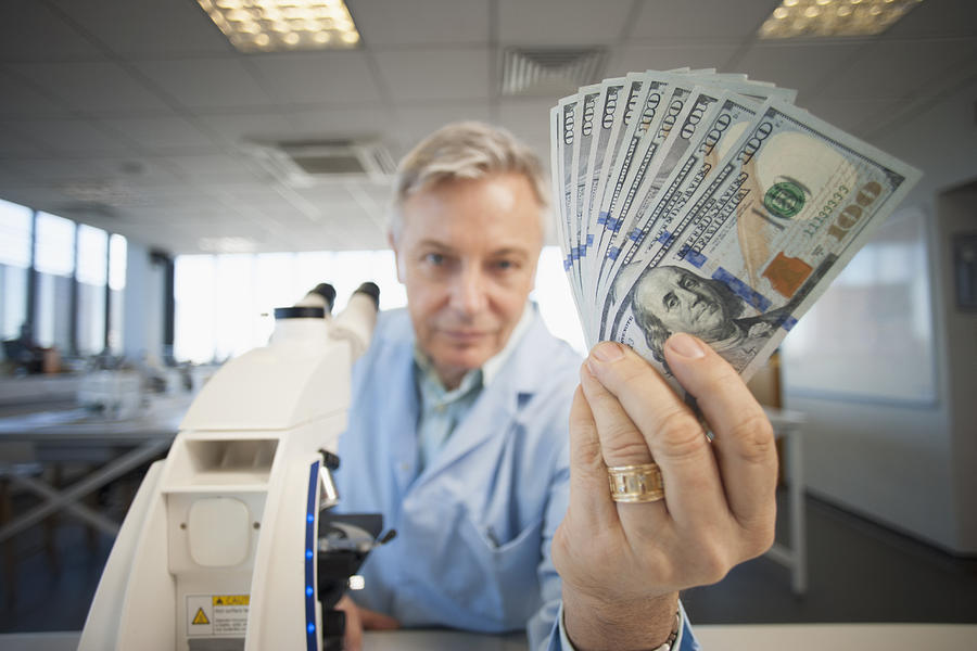 Caucasian scientist holding wad of money in lab Photograph by ER Productions Limited
