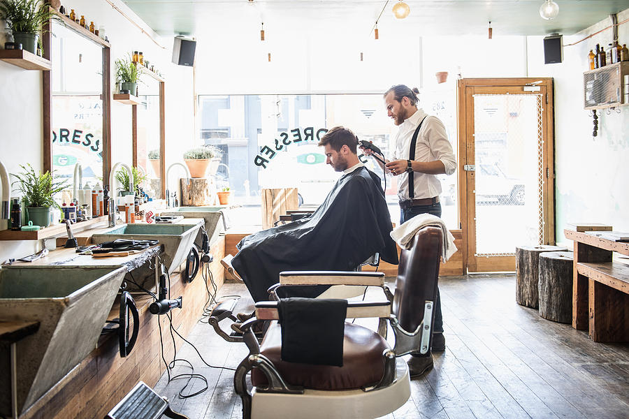 Caucasian stylist cutting hair of customer in barber shop Photograph by Jacobs Stock Photography Ltd