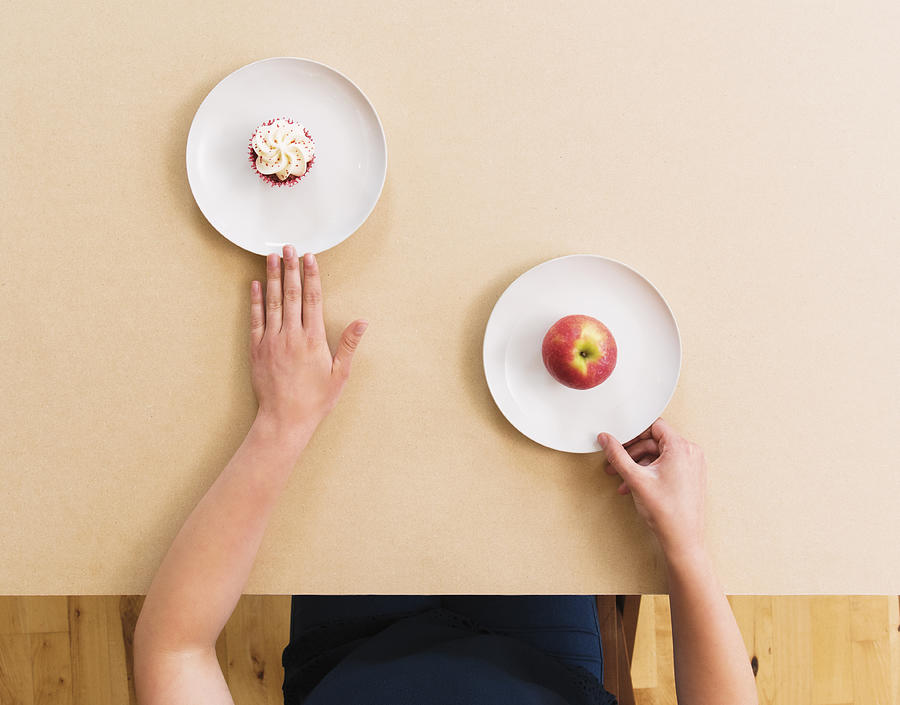 Caucasian woman choosing apple instead of cupcake at table Photograph by Jacobs Stock Photography Ltd