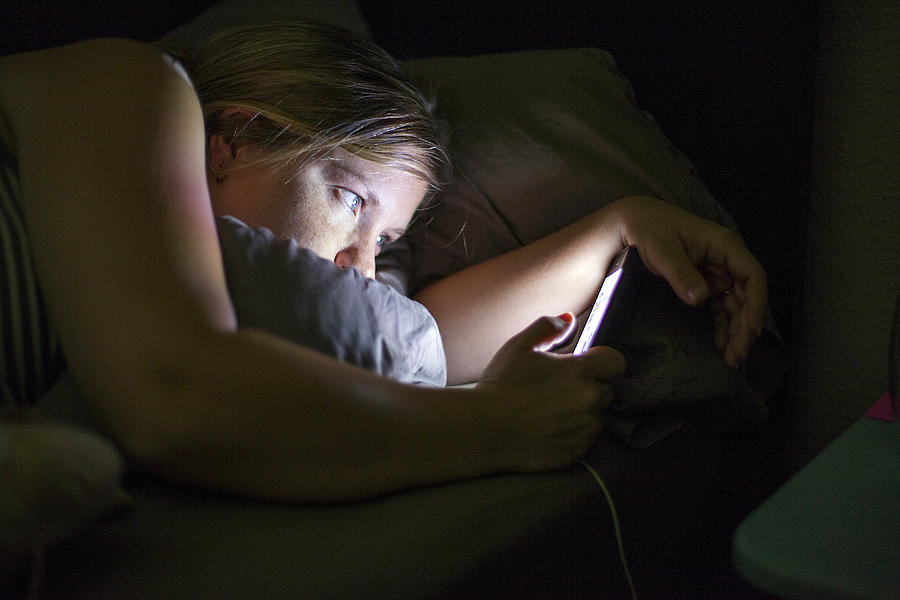 Caucasian woman using cell phone in bed Photograph by Adam Hester