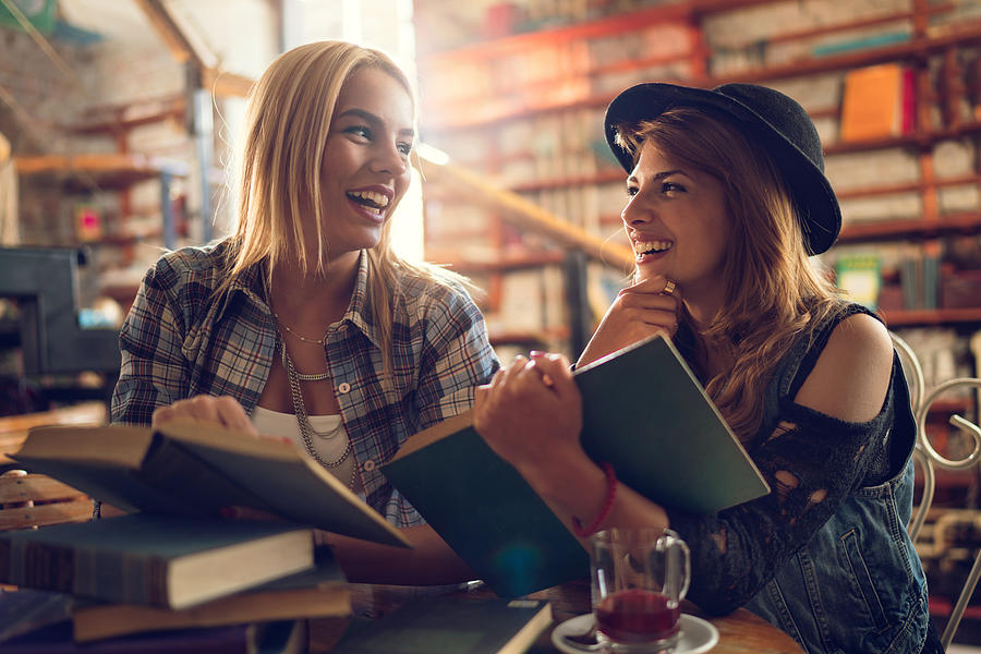 Cheerful female students talking to each other in a library. Photograph by BraunS