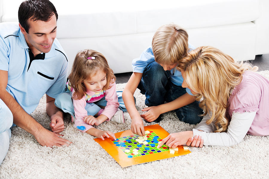 Cheerful parents playing board game with their children. Photograph by Skynesher
