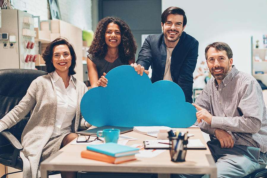 Cheerful team of professionals holding a big blue cloud Photograph by Pixelfit
