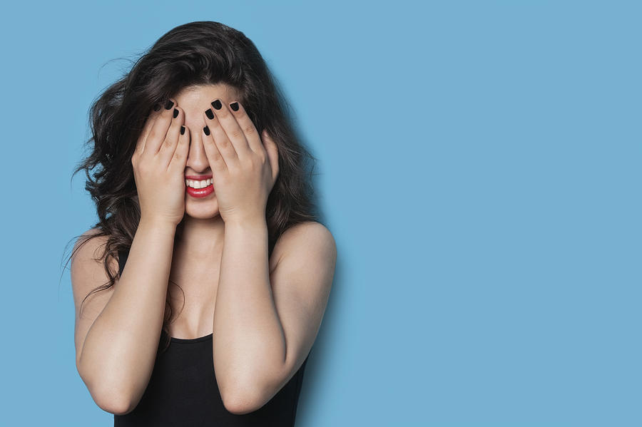Cheerful young woman covering her face against blue background Photograph by Moodboard